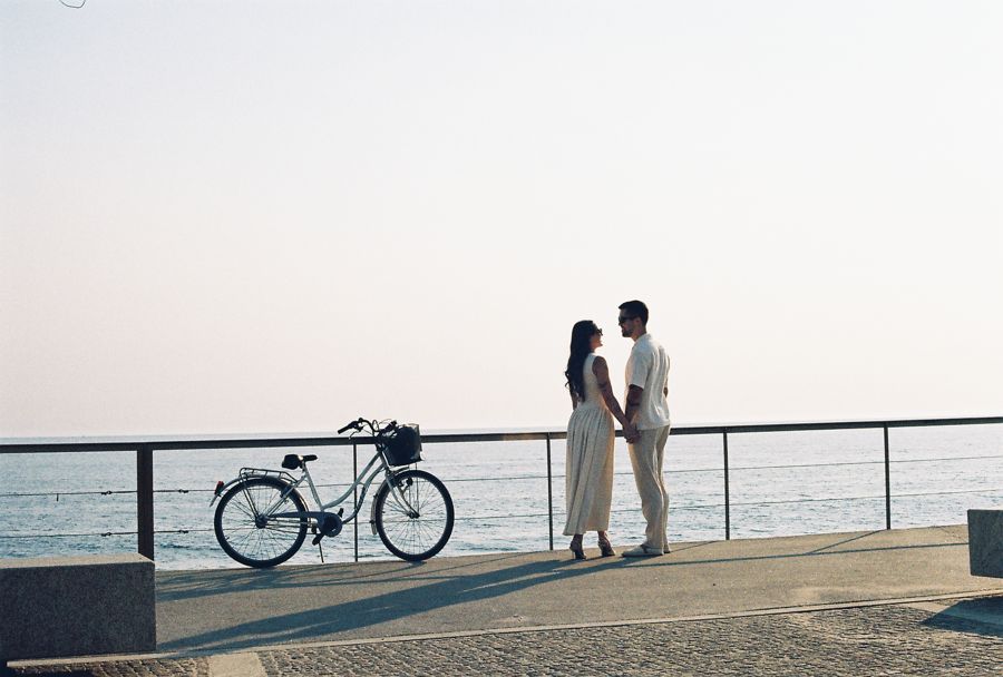Casal de mãos dadas junto a uma bicicleta, em frente ao mar